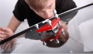 A person closely inspects a glass crack surface using a red repair tool, with reflections visible on the glossy surface.
